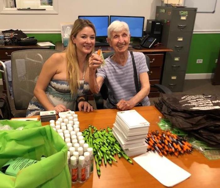 Two woman in a office with SERVPRO pens, paper, and bottles