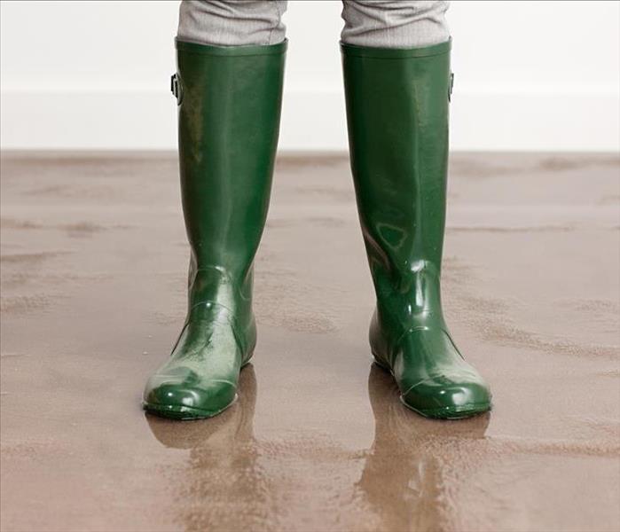 A person with green rain boots on standing on wet carpeting.  