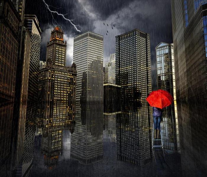 A woman in a blue suite on ladder with a red umbrella shielding rain drops in front of a cityscape
