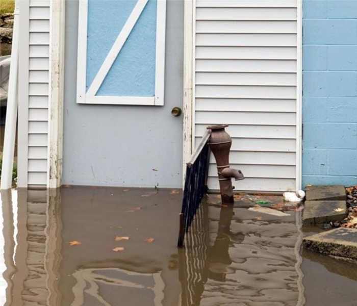 the front door of a house that is flooded with water three quarters up the doorway and covering the stairs leading up to it