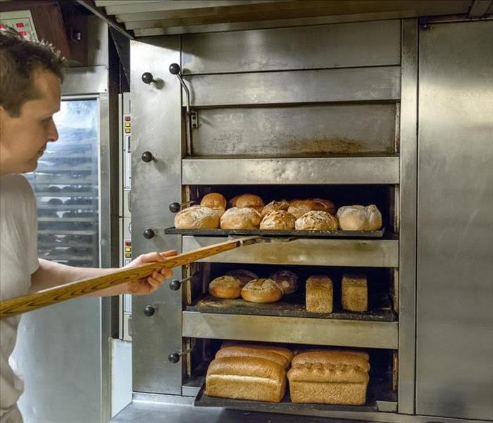 A man pulling bread out of a commercial oven 